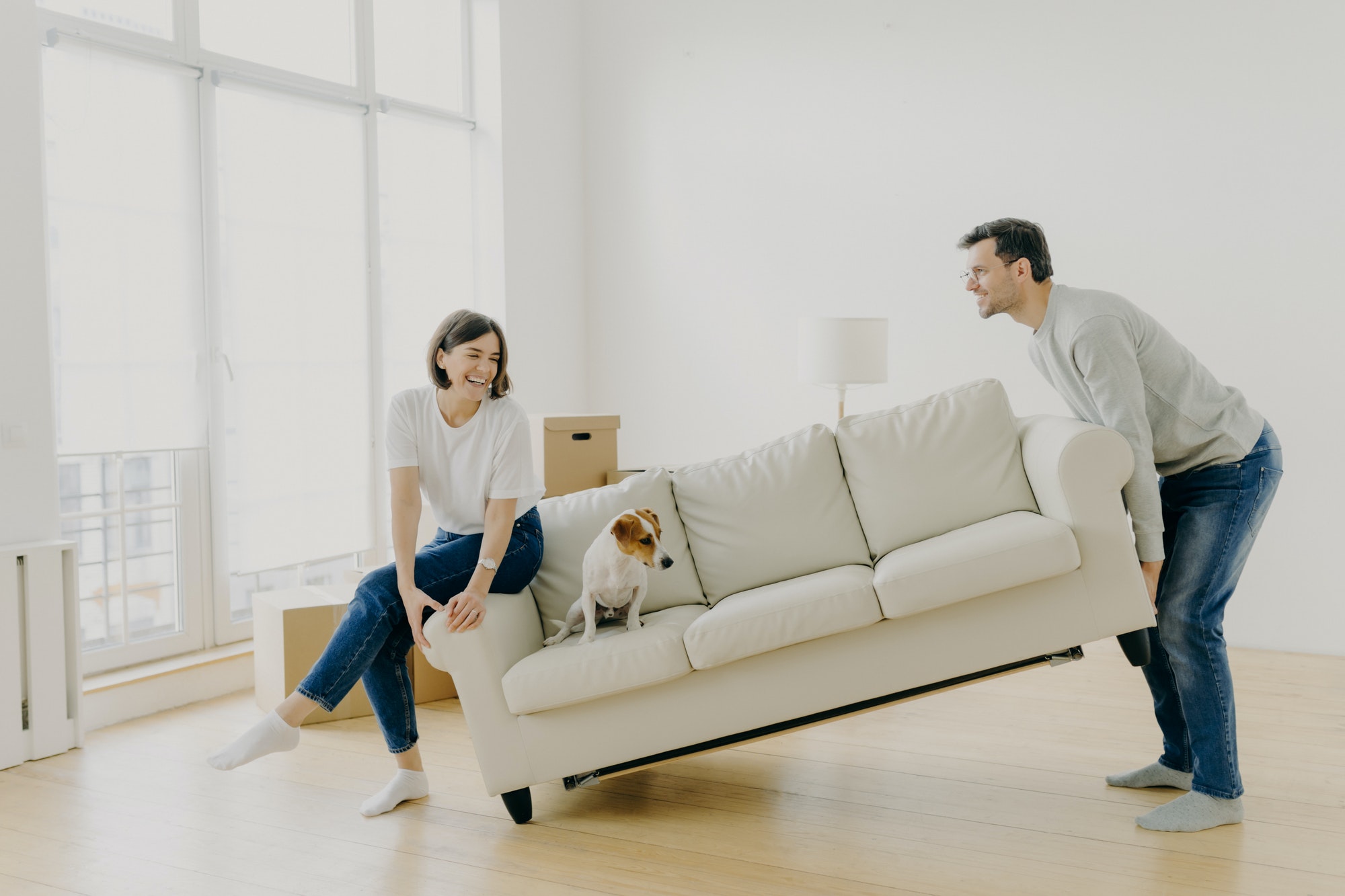 Husband and wife place sofa in living room, furnish their first home, help each other in renovation