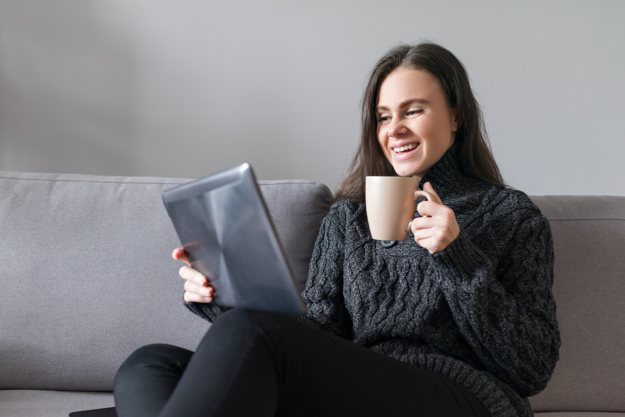 Young woman sitting at home on couch with gadgets